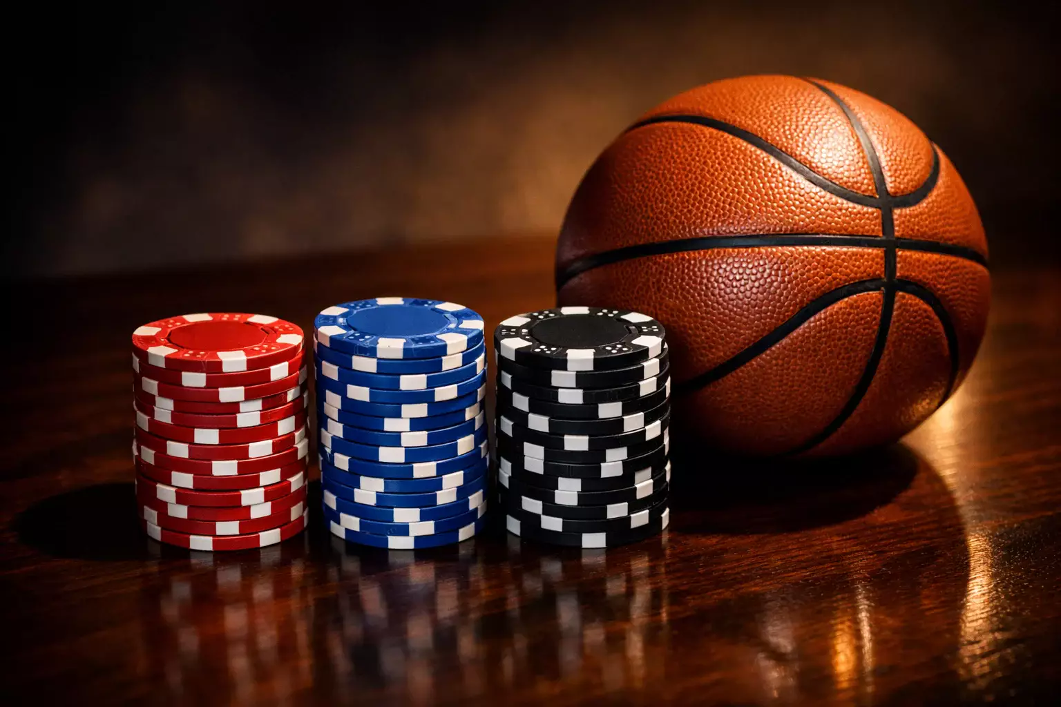 Gestapelte Jetons neben einem Basketball auf einem polierten Holztisch